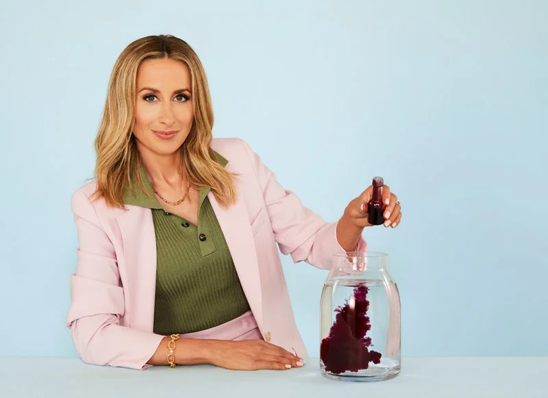 Dr Julie Smith in a pink jacket demonstrating a psychology experiment with ink in a jar of water